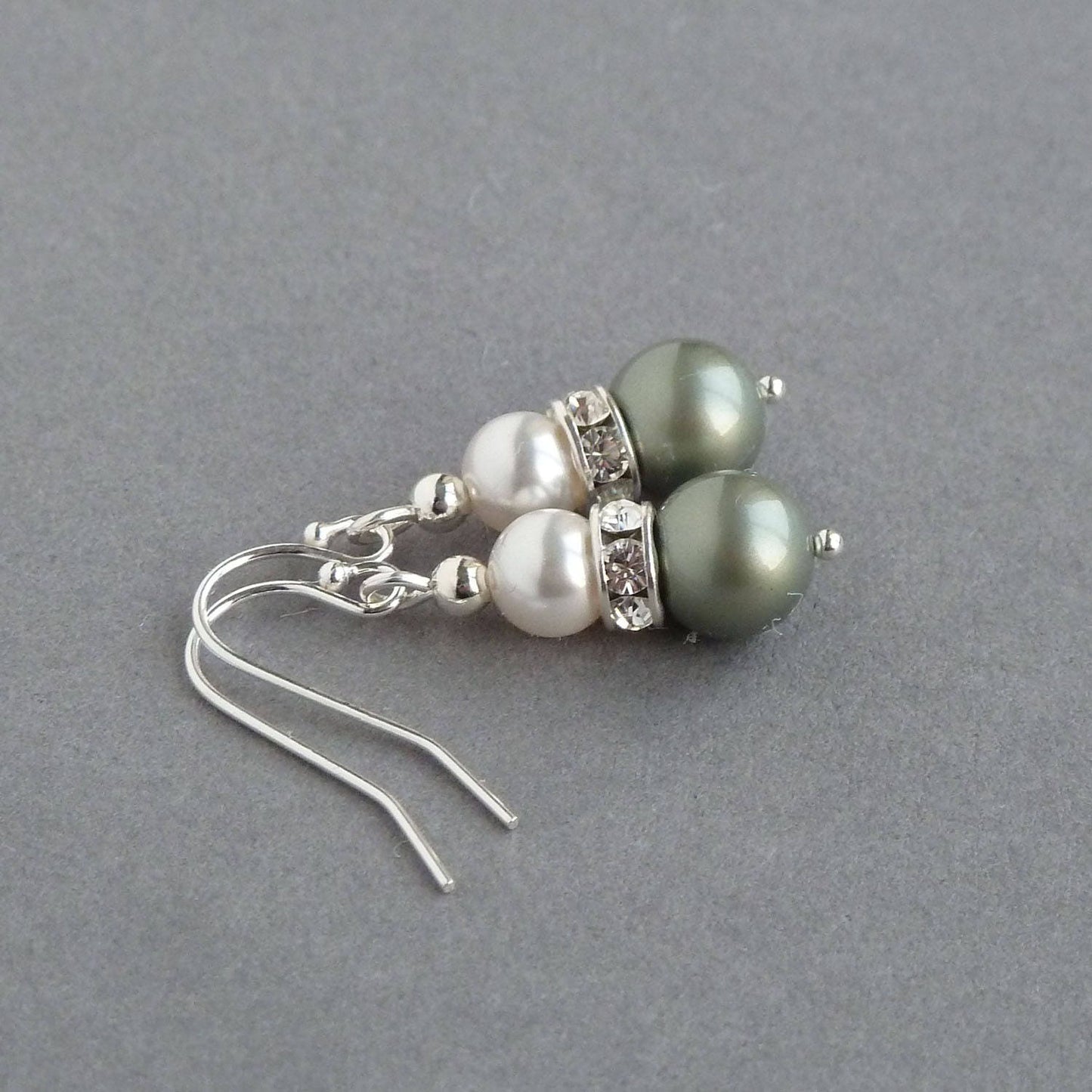 A white pearl sits in a crystal band above a sage green pearl to create a tear drop shaped pair of earrings.